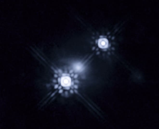 This picture shows a quasar that has been gravitationally lensed by a galaxy in the foreground, which can be seen as a faint shape around the two bright images of the quasar. Observations of one of the images show variations in colour over time. This is caused by stars within the lens galaxy passing through the path of the light from the quasar, magnifying the light from different parts of the quasarâs accretion disc as they move. This has allowed a team of scientists to reconstruct the colour and temperature profile of the accretion disc with unprecedented precision. The level of detail involved is equivalent to being able to study individual grains of sand on the surface of the Moon while standing on Earth. (c) NASA