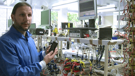 Dr Ioannis Ieropoulos inside the Bioenergy laboratory at the BRL, holding a phone powered by a microbial fuel cell stack. (c) Bristol University