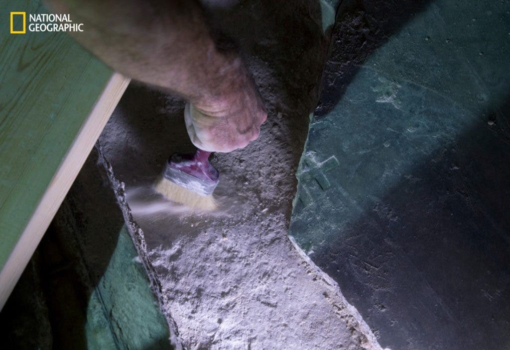 An expert carefully brushes away loose dust and dirt from the original limestone that's said to be the tomb of Jesus Christ. The small cross was etched during the Crusades. Credit: ODED BALILTY / NATIONAL GEOGRAPHIC