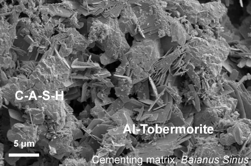 This microscopic image shows the lumpy calcium-aluminum-silicate-hydrate (C-A-S-H) binder material that forms when volcanic ash, lime, and seawater mix. Platy crystals of Al-tobermorite have grown amongst the C-A-S-H cementing matrix. Credit: Marie Jackson.