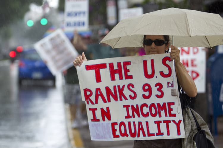 Woman protesting at an event holding sign that reads "The U.S. ranks 93rd in income equality".