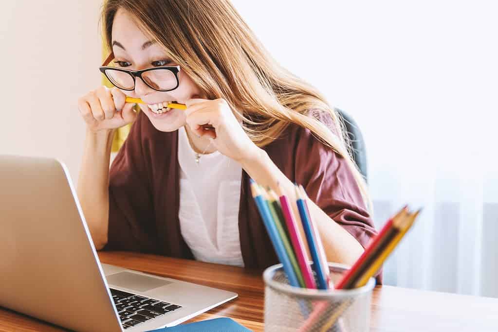 Female student studying in front of laptop while biting pencil.